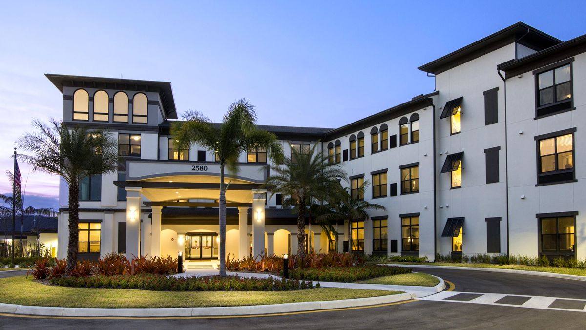 A beautiful residential building with well-maintained landscaping and palm trees, seen in the evening light.