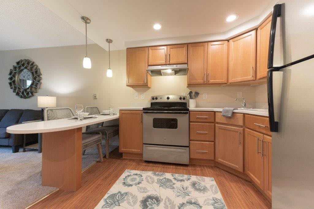 A modern kitchen with wooden cabinets, featuring stainless steel appliances and a cozy rug.