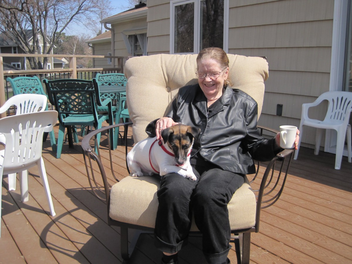 A woman sitting on a deck chair with a dog on her lap enjoying a sunny day.