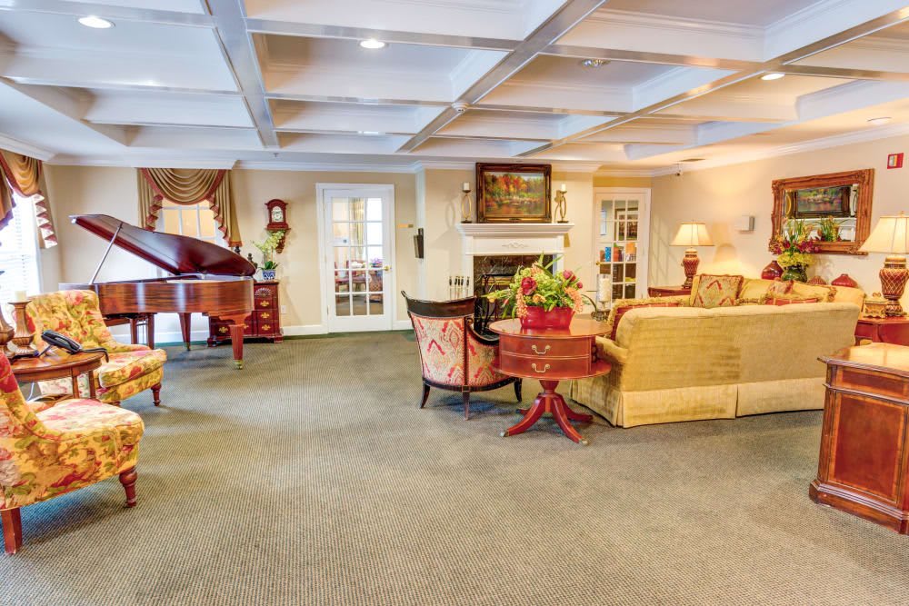 A spacious and elegantly decorated living room featuring a grand piano, fireplace, and cozy seating arrangement.