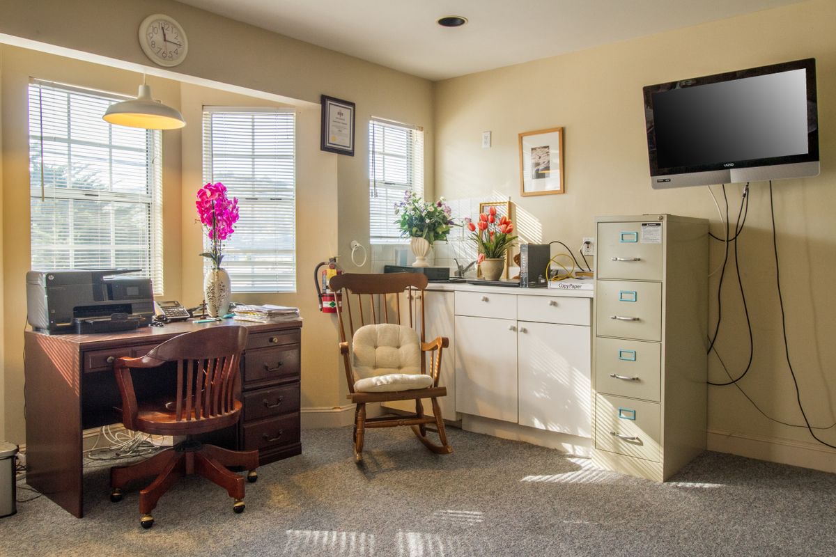 A cozy office space with a desk, rocking chair, and filing cabinet, illuminated by sunlight streaming through the windows.