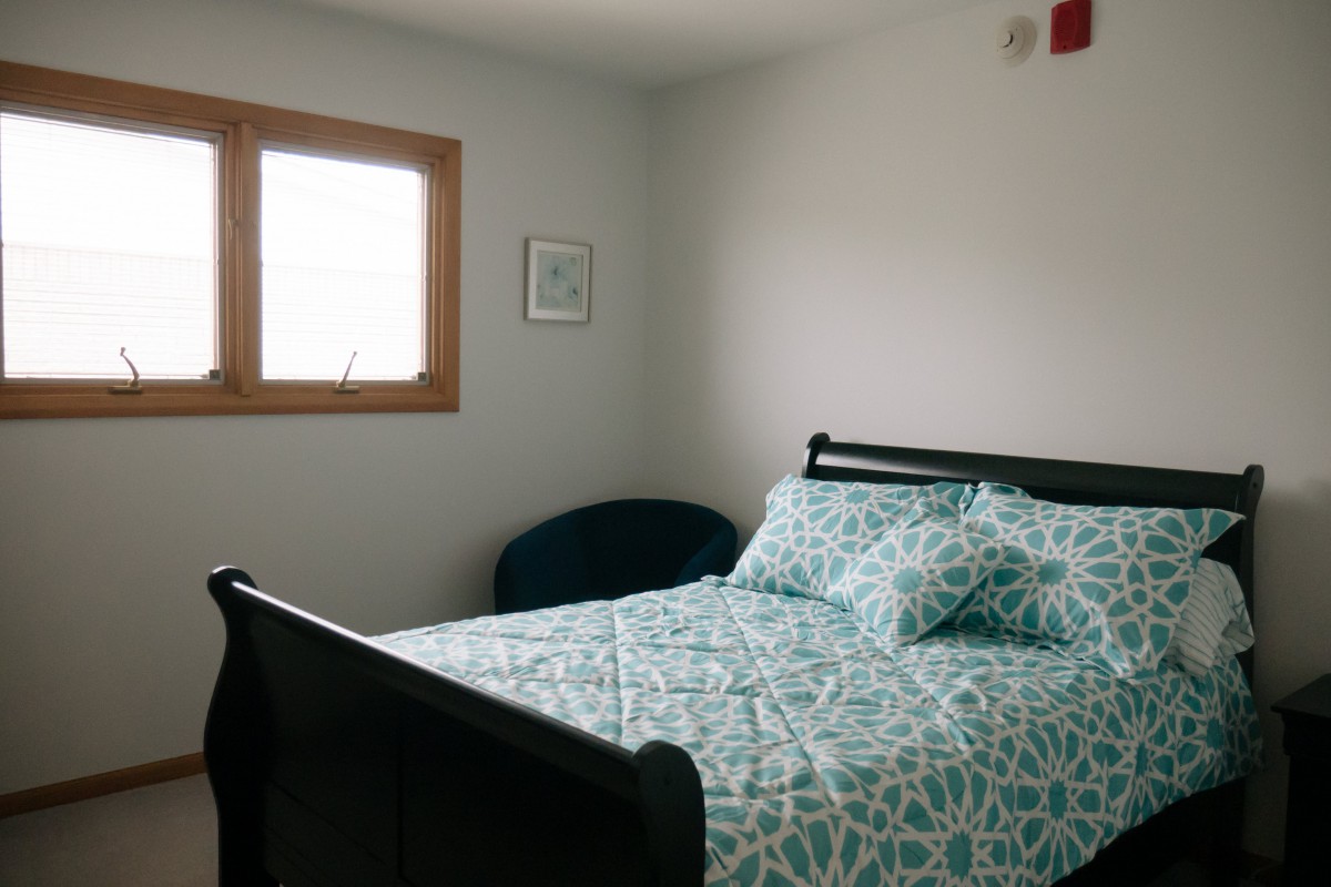 A cozy bedroom with a patterned bedspread and natural light from the window.