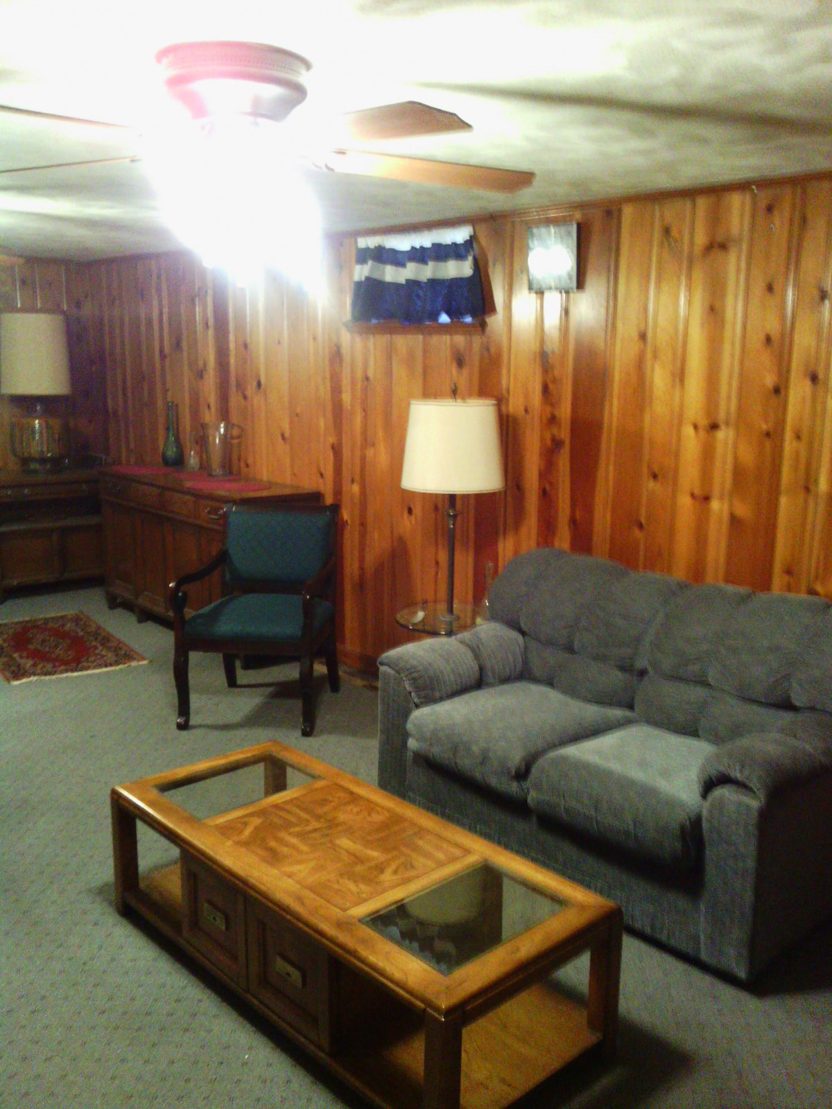 A cozy living room with wood paneling, featuring a sofa, armchair, and coffee table.