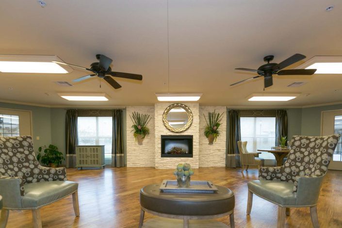 A spacious living room with elegant decor, featuring a central fireplace, ceiling fans, and ample seating.