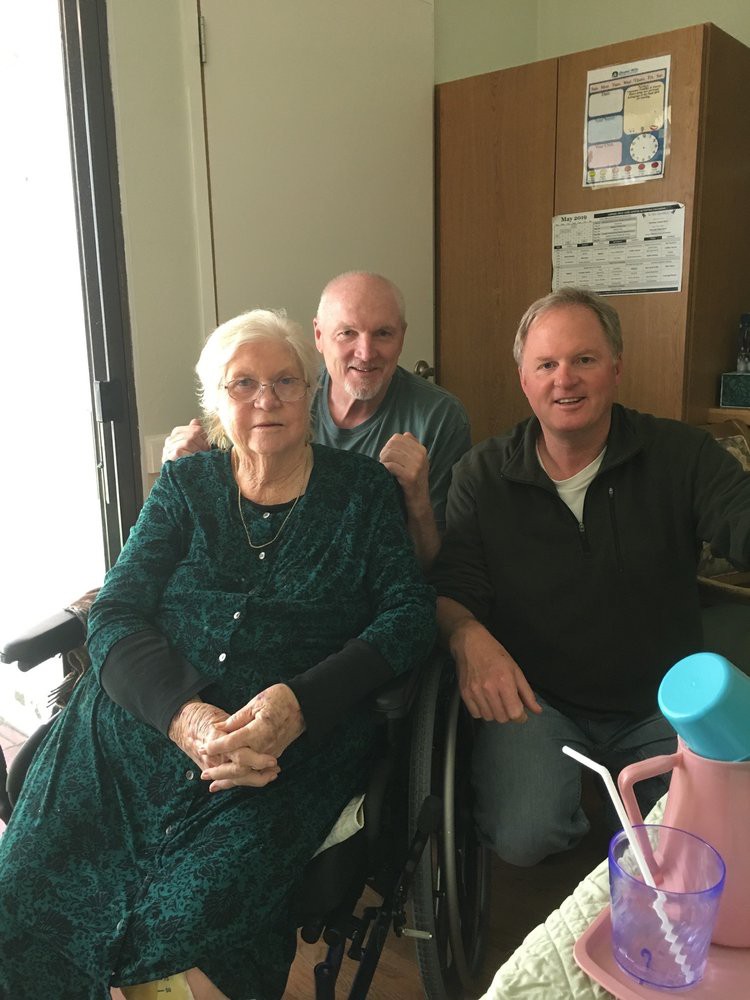 An elderly woman sitting with two men in an indoor setting.