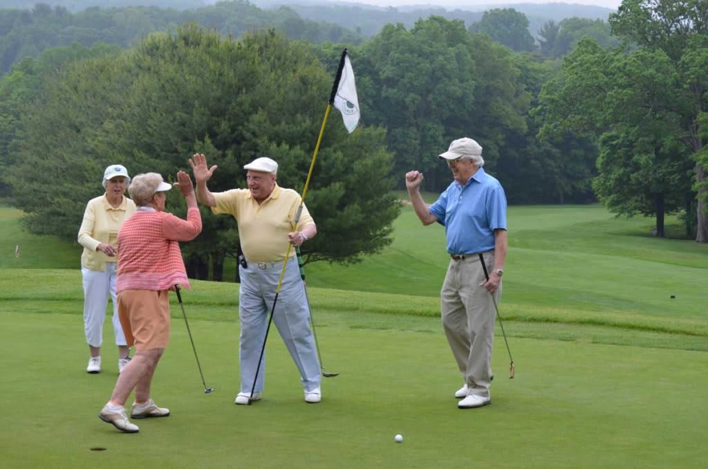 A group of seniors celebrates a successful golf shot on a lush golf course.