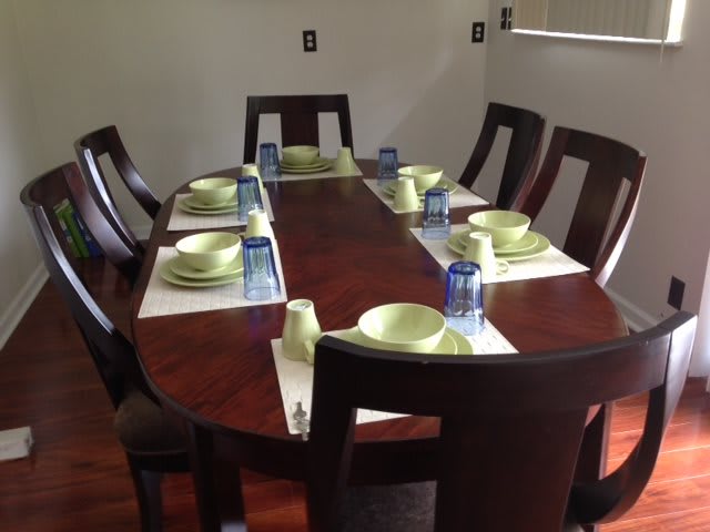 A neatly set dining table with green plates and blue glasses, surrounded by wooden chairs.