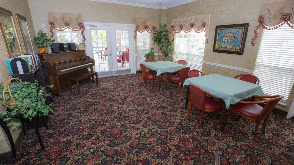 A comfortable room with tables, chairs, a piano, and large windows.
