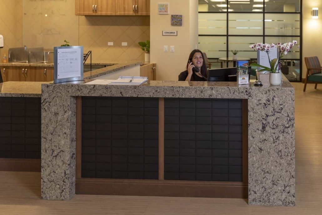 A receptionist sits at a front desk, speaking on the telephone in an office environment.