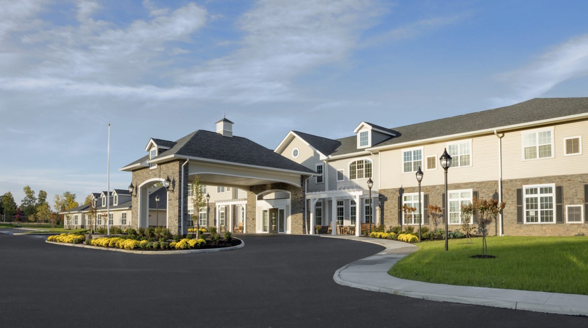 A large residential building with a covered entrance and landscaped surroundings under a clear blue sky.