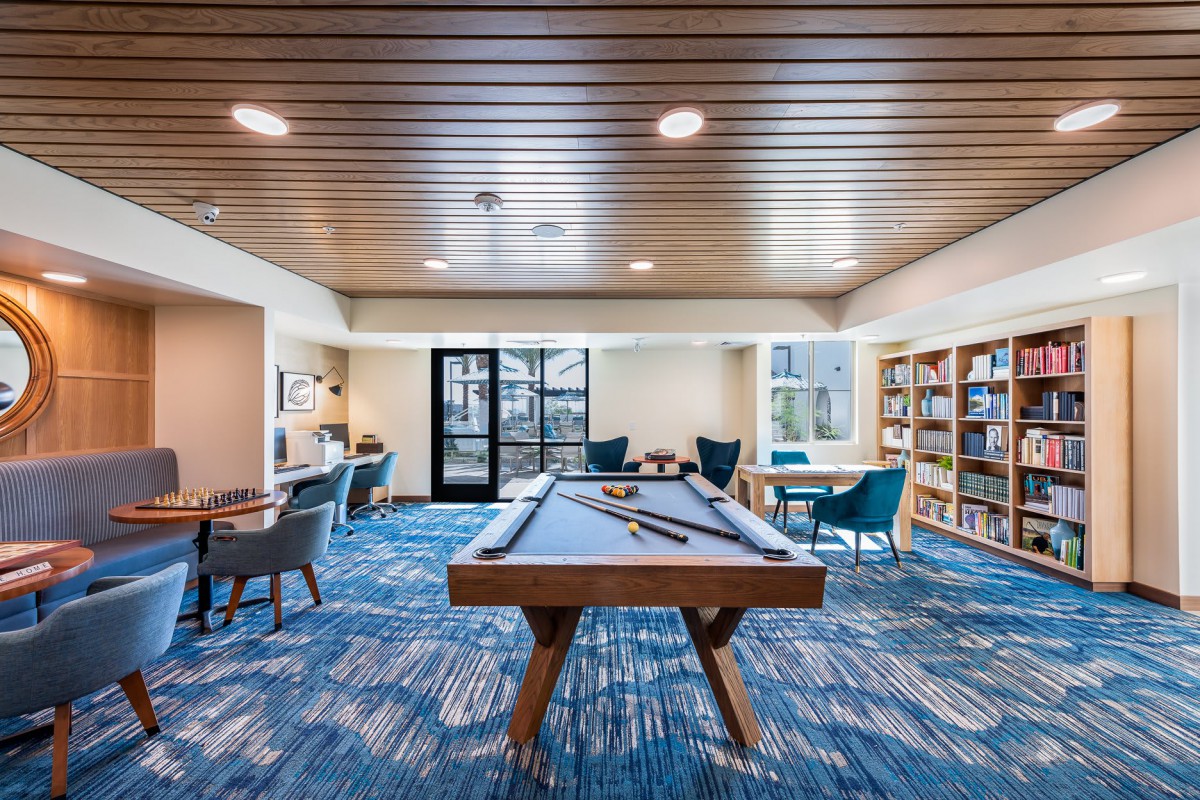 A modern recreation room featuring a pool table, bookshelves, and a comfortable seating area.