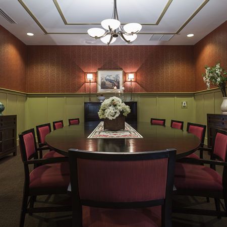 A well-appointed meeting room featuring a round conference table with red upholstered chairs and elegant lighting.