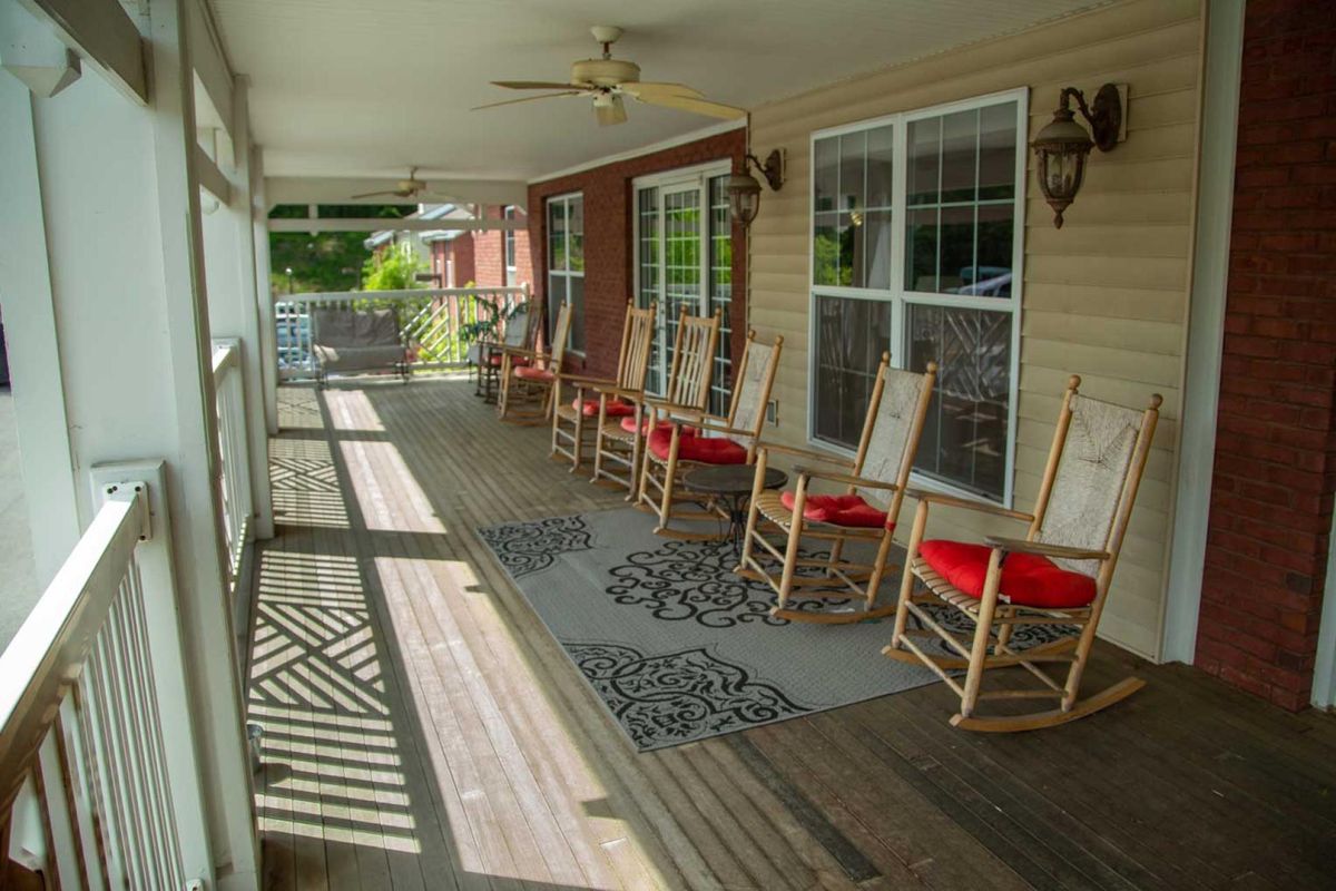 A cozy covered porch with a row of rocking chairs and decorative rugs.