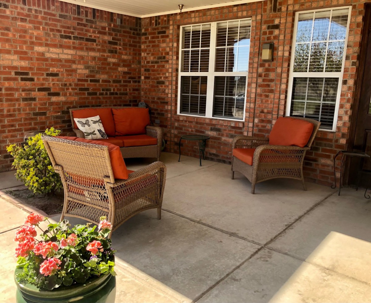 A cozy patio with wicker furniture and bright orange cushions, accented by potted plants and surrounded by brick walls.