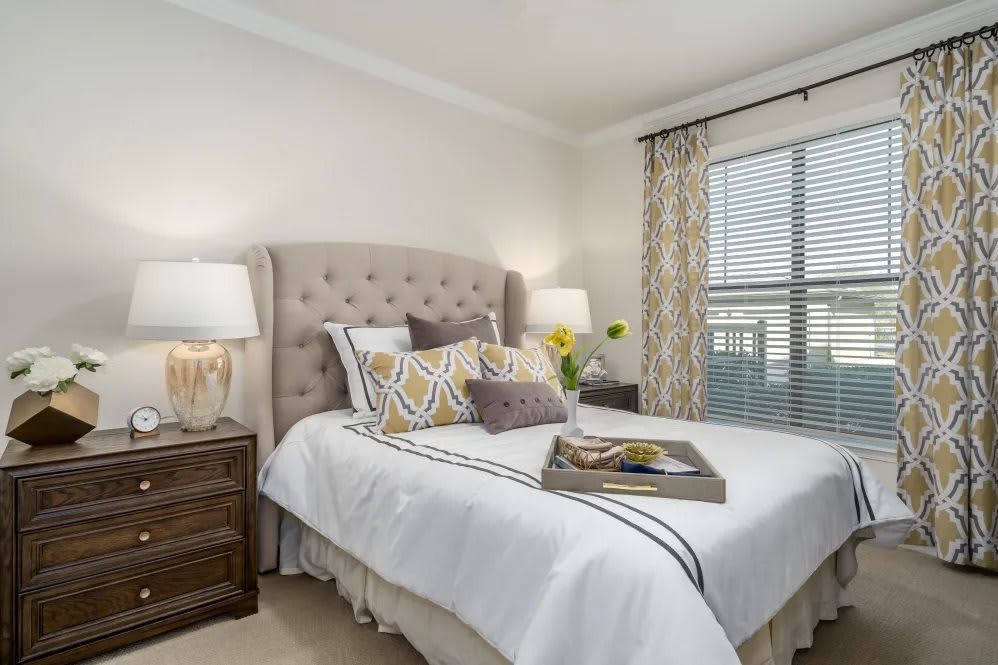 A cozy and elegantly designed bedroom featuring a tufted headboard, decorative pillows, and a wooden nightstand with lamps.