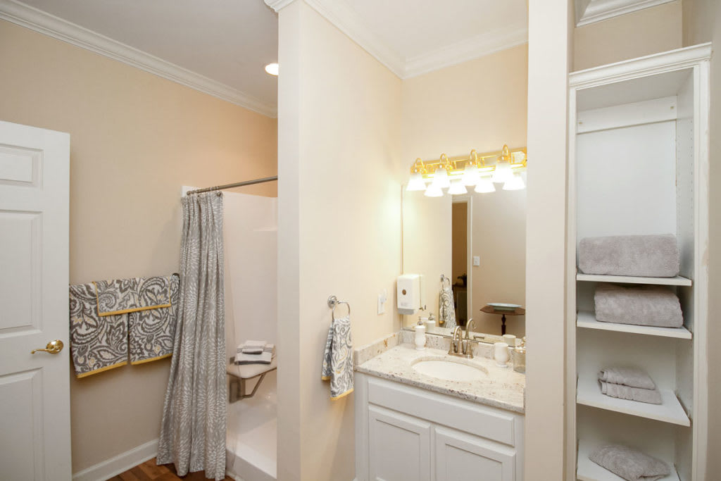 A well-lit bathroom with a sink, mirror, and shower area featuring neatly arranged towels.