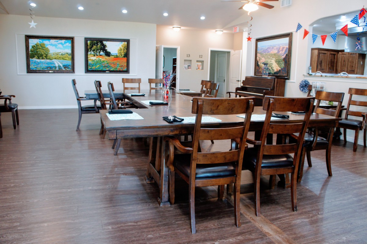 A spacious dining room with wooden chairs and tables, adorned with colorful artwork and a piano.