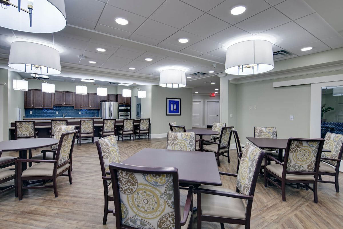 A modern dining area with tables and chairs, featuring a kitchen in the background.