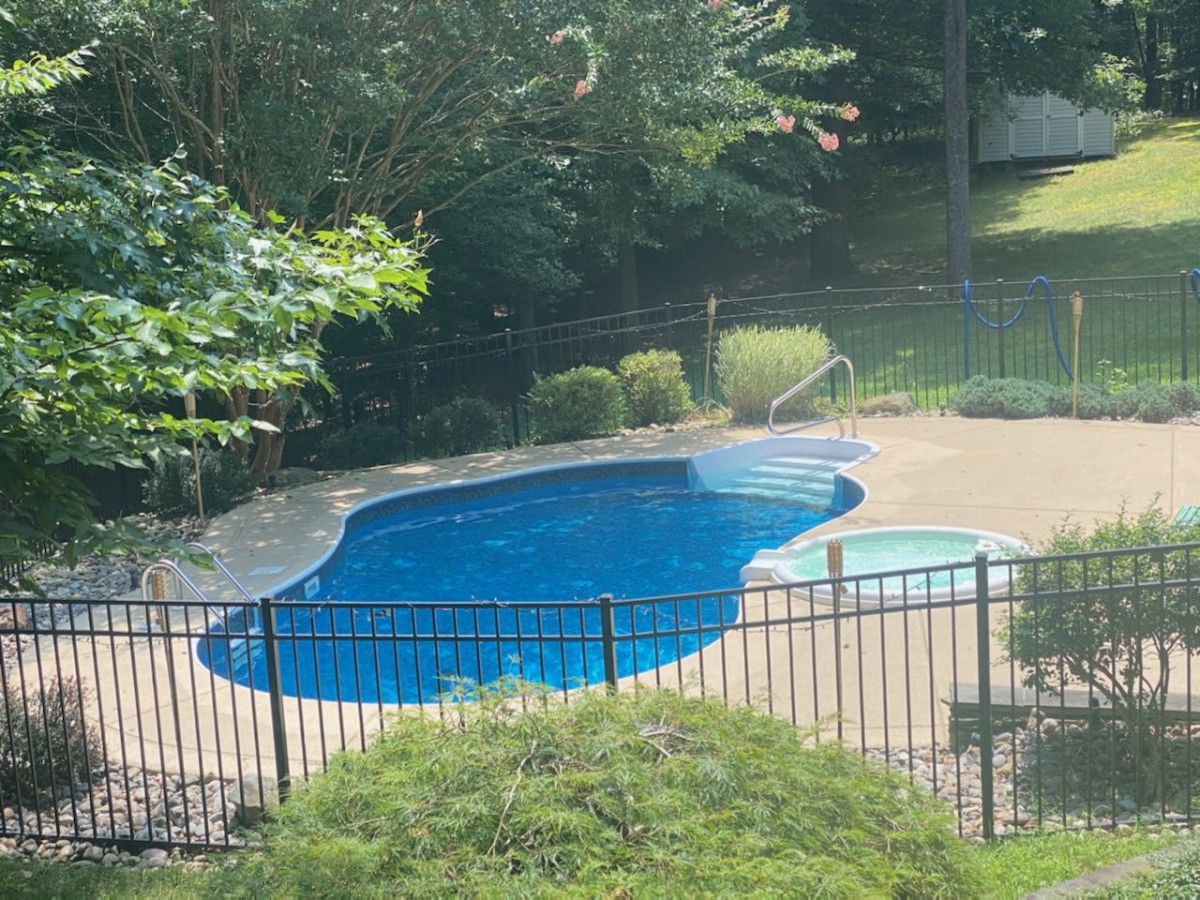 A serene backyard swimming pool surrounded by greenery and a safety fence.