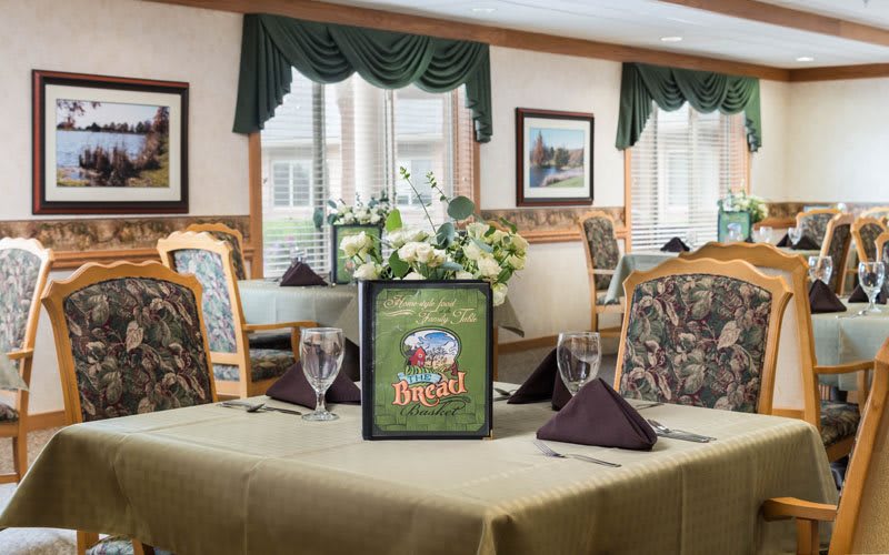 A neatly set dining table in a restaurant with floral centerpiece and menu display.