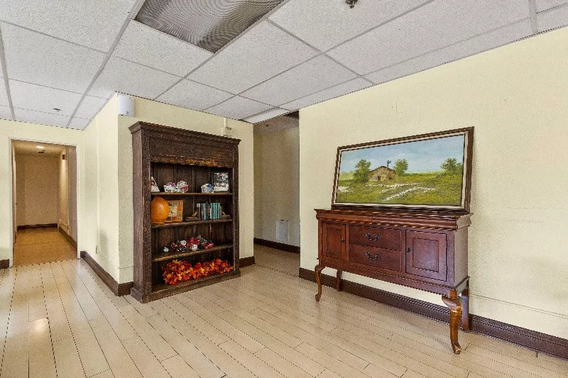 A room interior with wooden furniture, featuring a cabinet filled with decorative items and a painting above a sideboard.