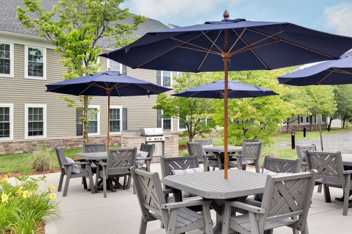 A patio area with tables and chairs under large blue umbrellas, set in a garden setting.