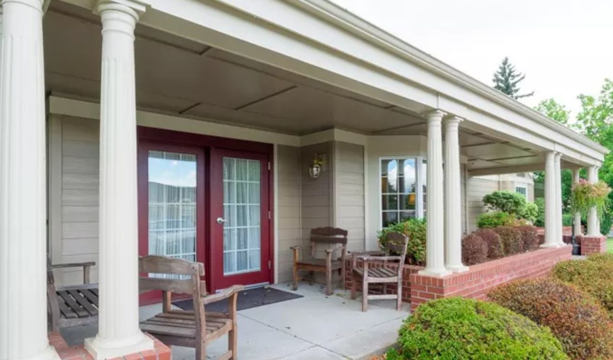 A cozy front porch with chairs, a red double door, and decorative columns.