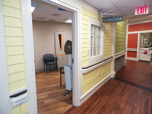 A view of a hospital corridor featuring yellow walls and a wooden floor, leading to a waiting area.