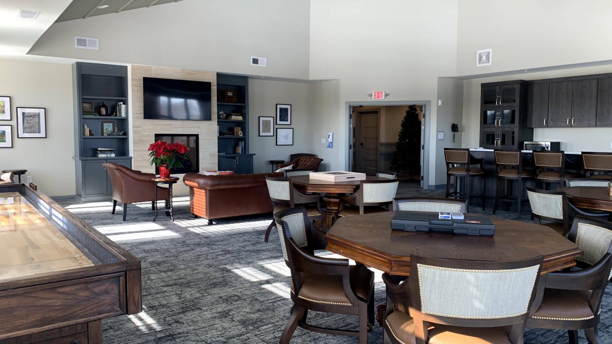 A modern lobby area with tables, chairs, a television, and large windows letting in natural light.