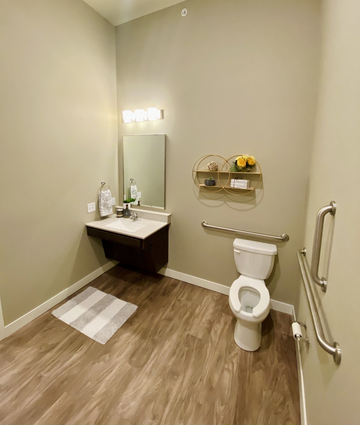 A clean and spacious bathroom with a toilet, sink, mirror, and handrail for accessibility.