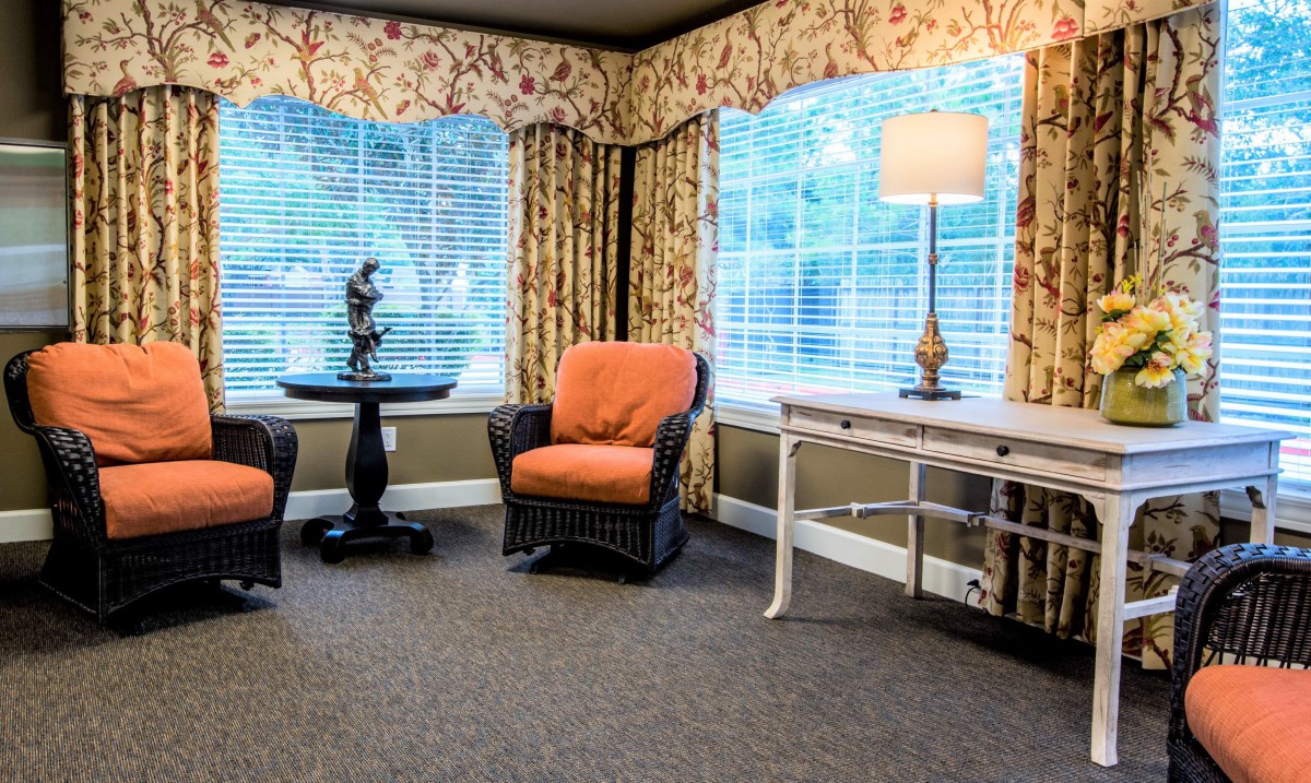 A cozy living room corner with wicker chairs, a side table, and a lamp by the window.