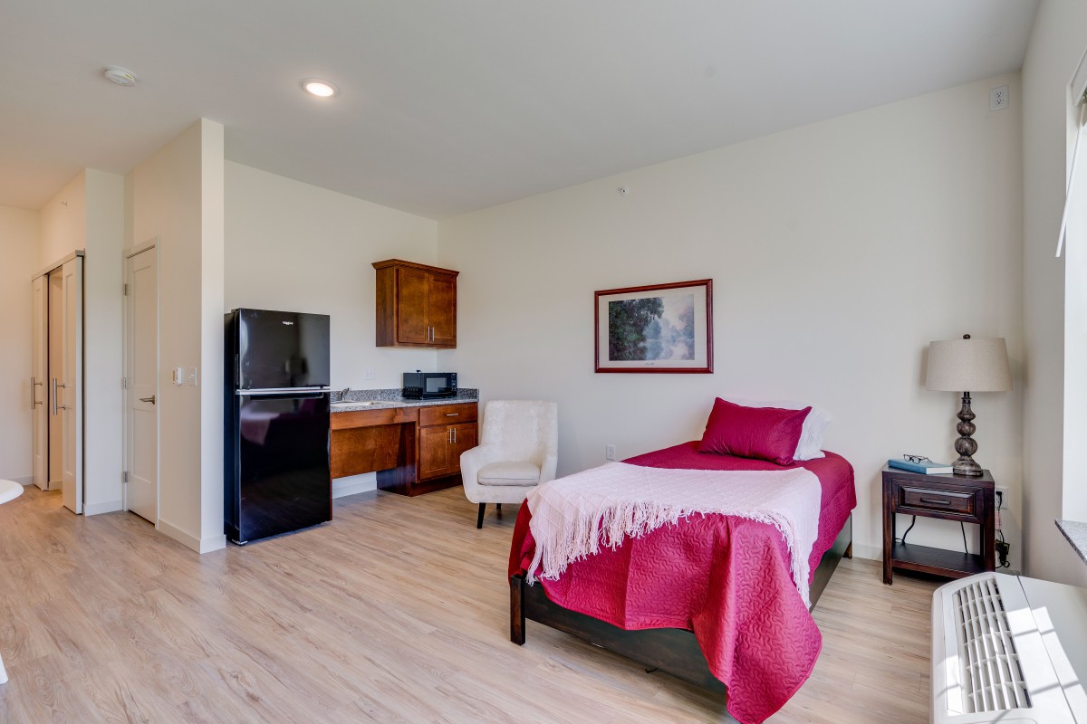 A minimalist bedroom with a single bed and a small kitchenette.