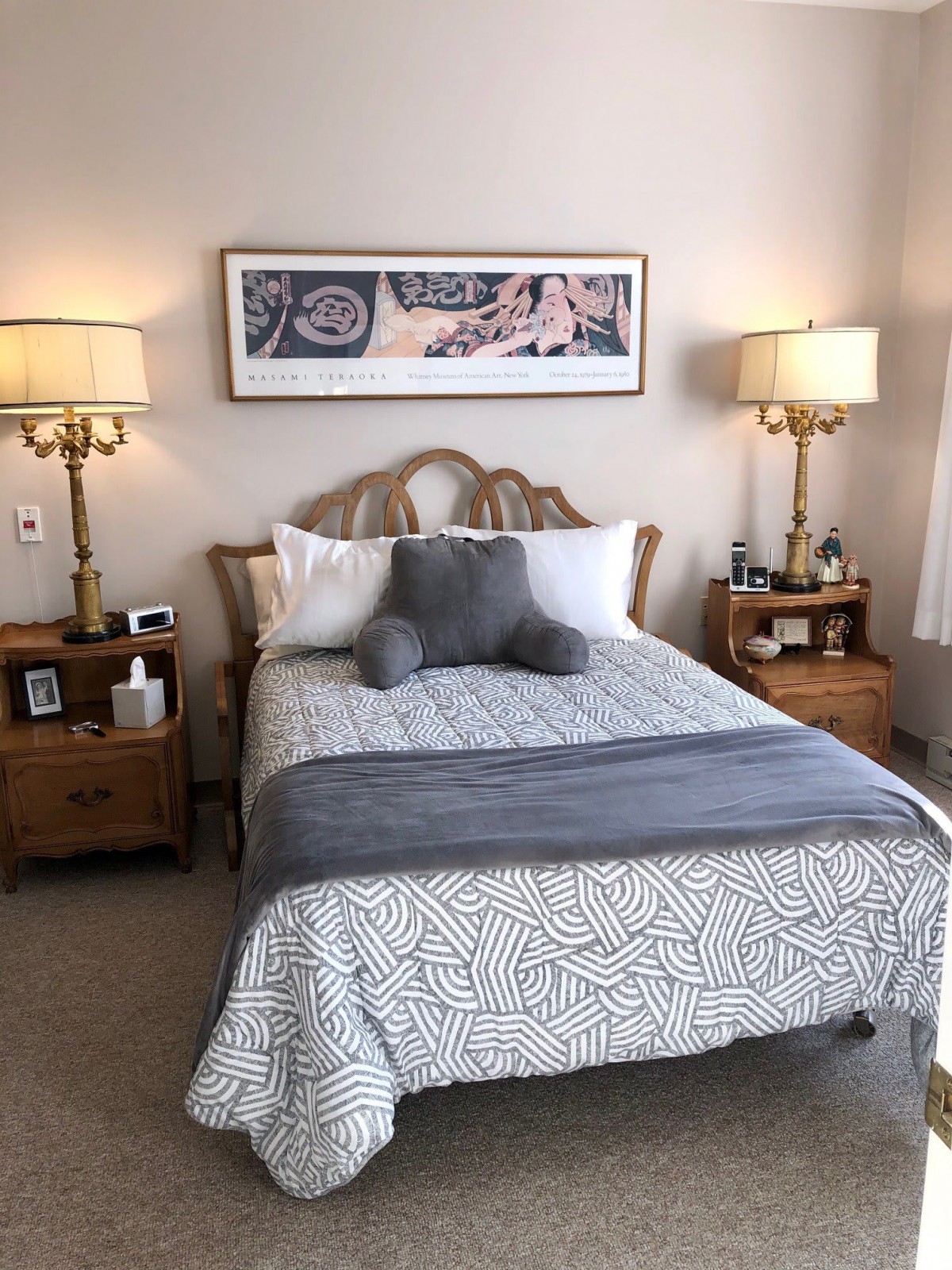 A cozy bedroom with a neatly made bed, flanked by two nightstands and elegant lamps, and artwork hanging above.
