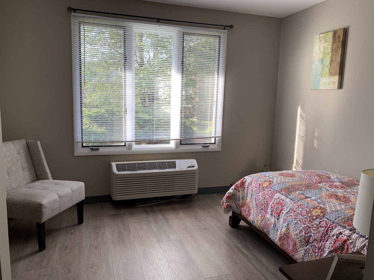 A cozy bedroom with a bed, chair, and large window letting in natural light.