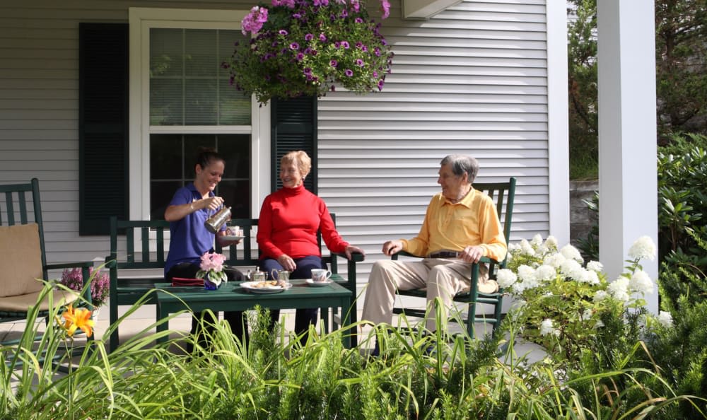 Three people enjoying a relaxing time together on a porch surrounded by flowers.