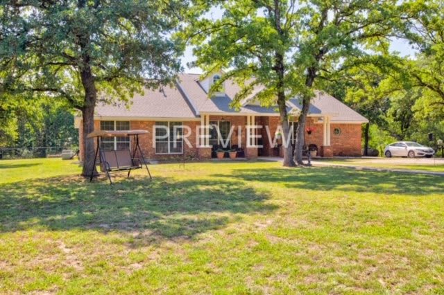 A brick house with a spacious backyard featuring trees and a swing.