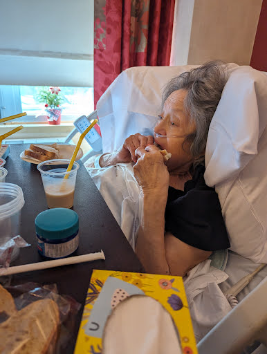 A senior person enjoying a snack in a hospital setting, surrounded by personal items.