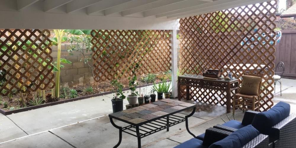 A cozy outdoor patio with a table, potted plants, and a lattice fence.