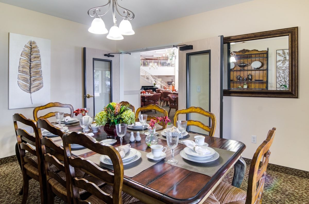 A dining room with a set table, featuring elegant tableware and a floral centerpiece.