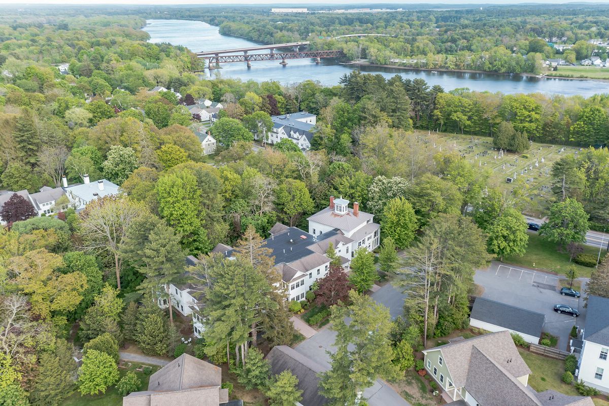 Aerial view of a lush, green neighborhood with houses surrounded by trees and a river in the background.