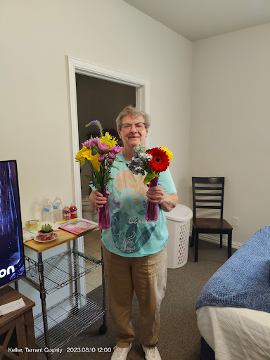 A cheerful woman holding vibrant bouquets of flowers in a cozy indoor setting.