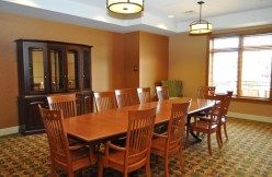 A spacious conference room with a large wooden table surrounded by chairs, featuring elegant lighting fixtures.