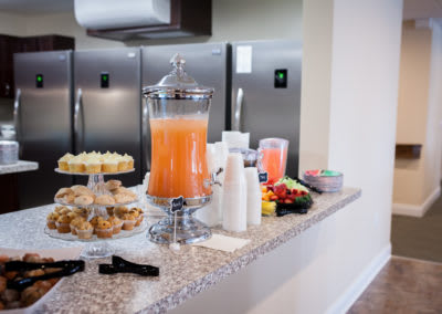 A countertop with a variety of refreshments, including a juice dispenser, pastries, and a fruit platter.