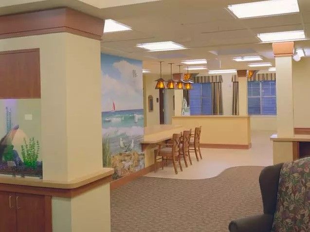 A cozy interior space featuring a mural, seating area with chairs and overhead lighting, and large windows with curtains.