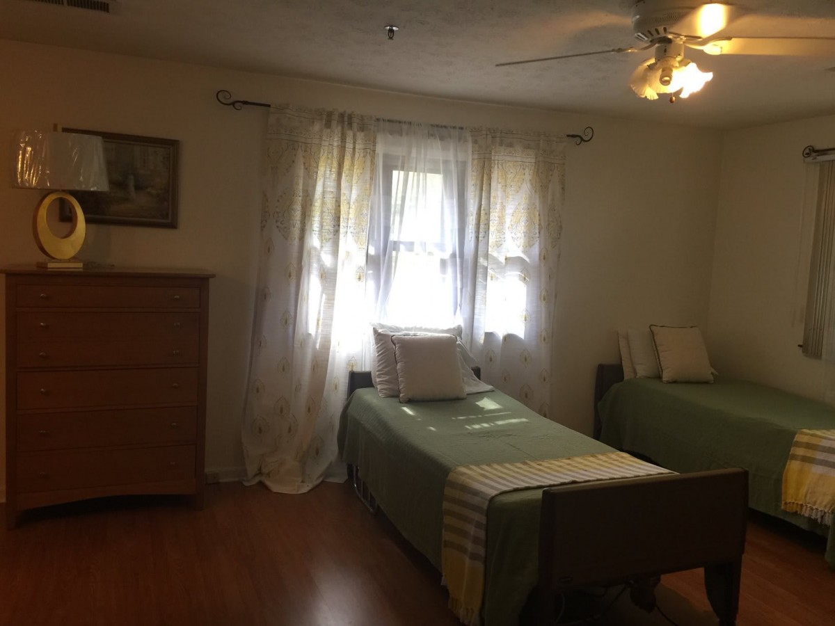 A cozy bedroom with twin beds, a wooden dresser, and soft light filtering through the curtains.