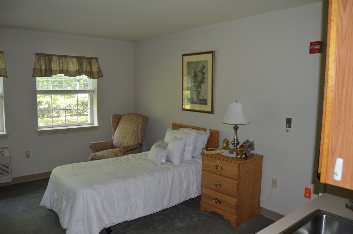 A cozy bedroom with a single bed, nightstand, and a chair by the window.
