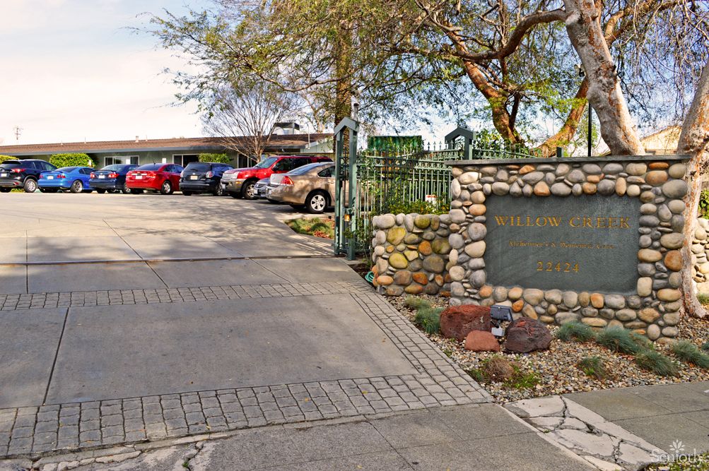 Entrance to a parking lot with a stone sign and surrounding trees.