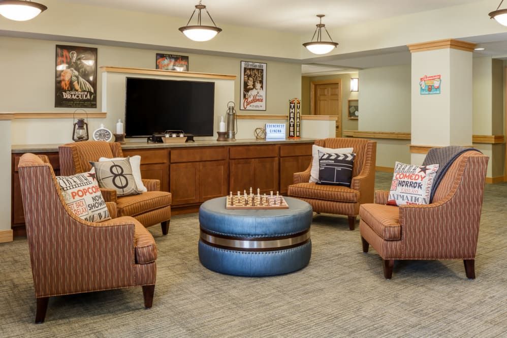 A cozy living room with comfortable armchairs, a central coffee table featuring a chessboard, and a television on the wall.