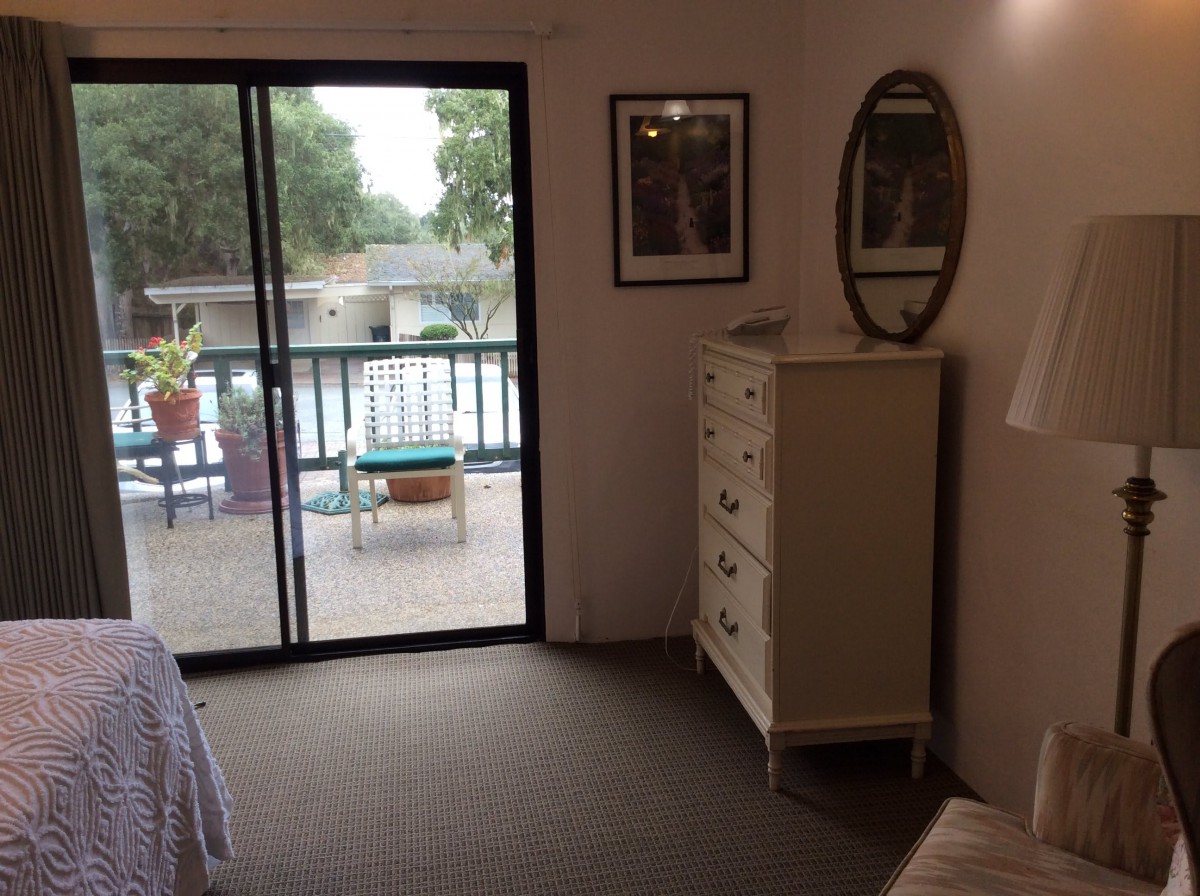 A cozy bedroom with a dresser and mirror, featuring a sliding door leading to a balcony.