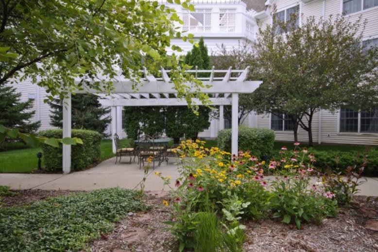 A charming outdoor garden area with a white pergola and seating surrounded by lush greenery and flowers.